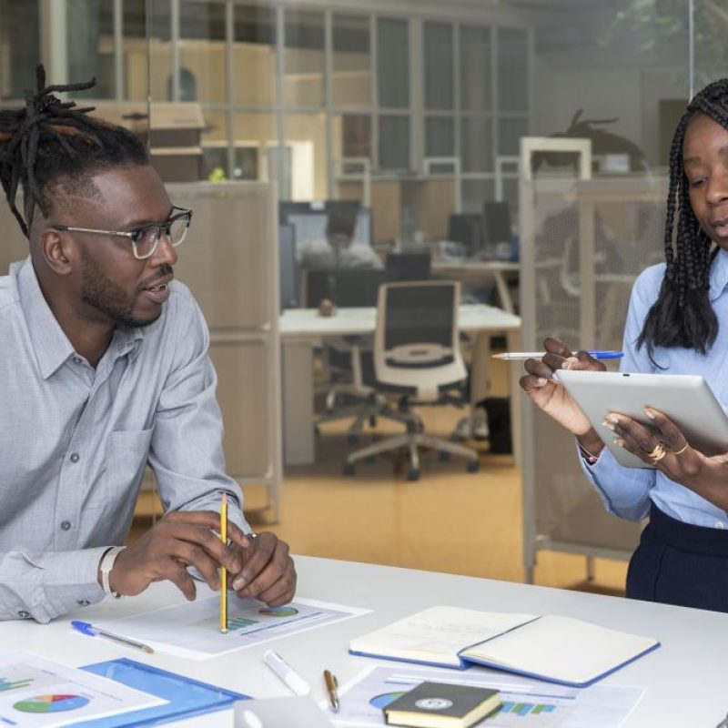 Two young African American entrepreneurs with a digital tablet and graphics on the table in a boardroom holding a meeting in the office. Talent